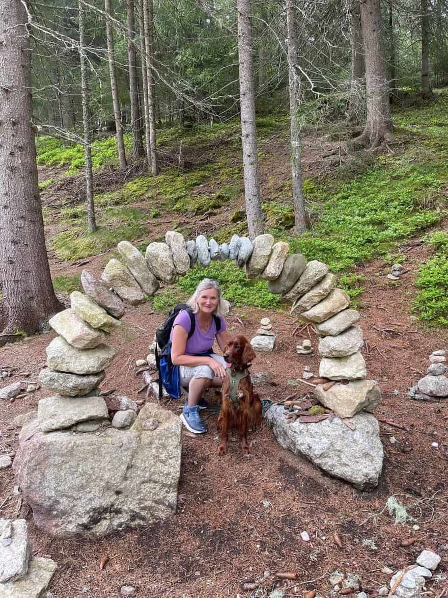 Irish Red Setter von Irish Windlooper's mit Besitzerin in einem Steinbogen aus gestapelten Steinen im Nadelwald